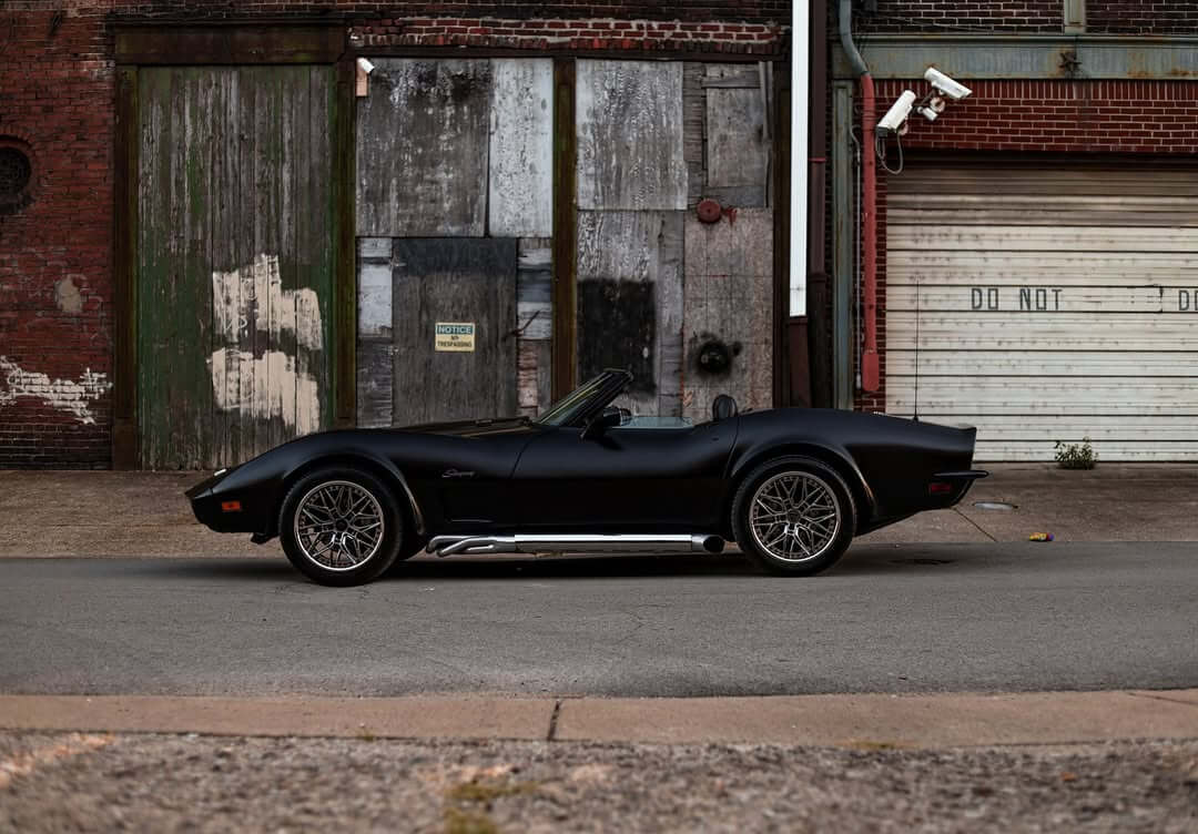Black 1973 C3 Corvette convertible with custom chrome and red aluminum wheels parked on a street.