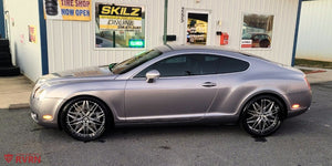 Side profile of a silver 2006 Bentley Continental GT on RVRN RV-T081 polished aluminum deep dish wheels outside a tire shop