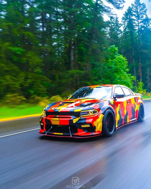 Dodge Charger with custom camouflage wrap and 20-inch black deep dish rims driving through a lush forest background.