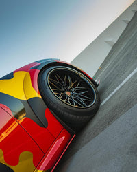 Close-up of a Dodge Charger featuring 20-inch black deep dish custom forged wheels on a colorful camo design.
