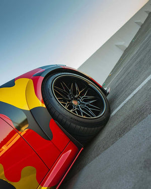 Close-up of a Dodge Charger featuring 20-inch black deep dish custom forged wheels on a colorful camo design.