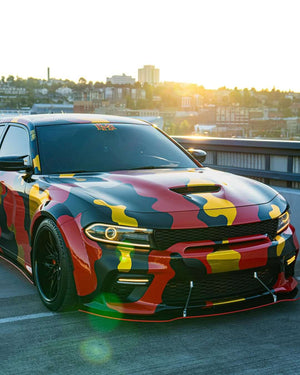 Dodge Charger with custom camouflage wrap and 20-inch black deep dish rims, parked with a city skyline in the background.