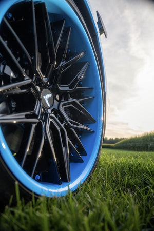 Close-up of the RVRN RV-T081 gloss black spoke and Rapid Blue lip wheel in the grass beside a 2025 Corvette C8 Z06
