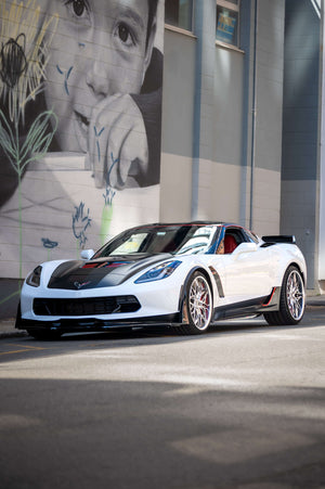 Front three-quarter view of a white 2015 Corvette C7 Z06 on RVRN RV-T081 deep dish wheels beside a large street-art mural